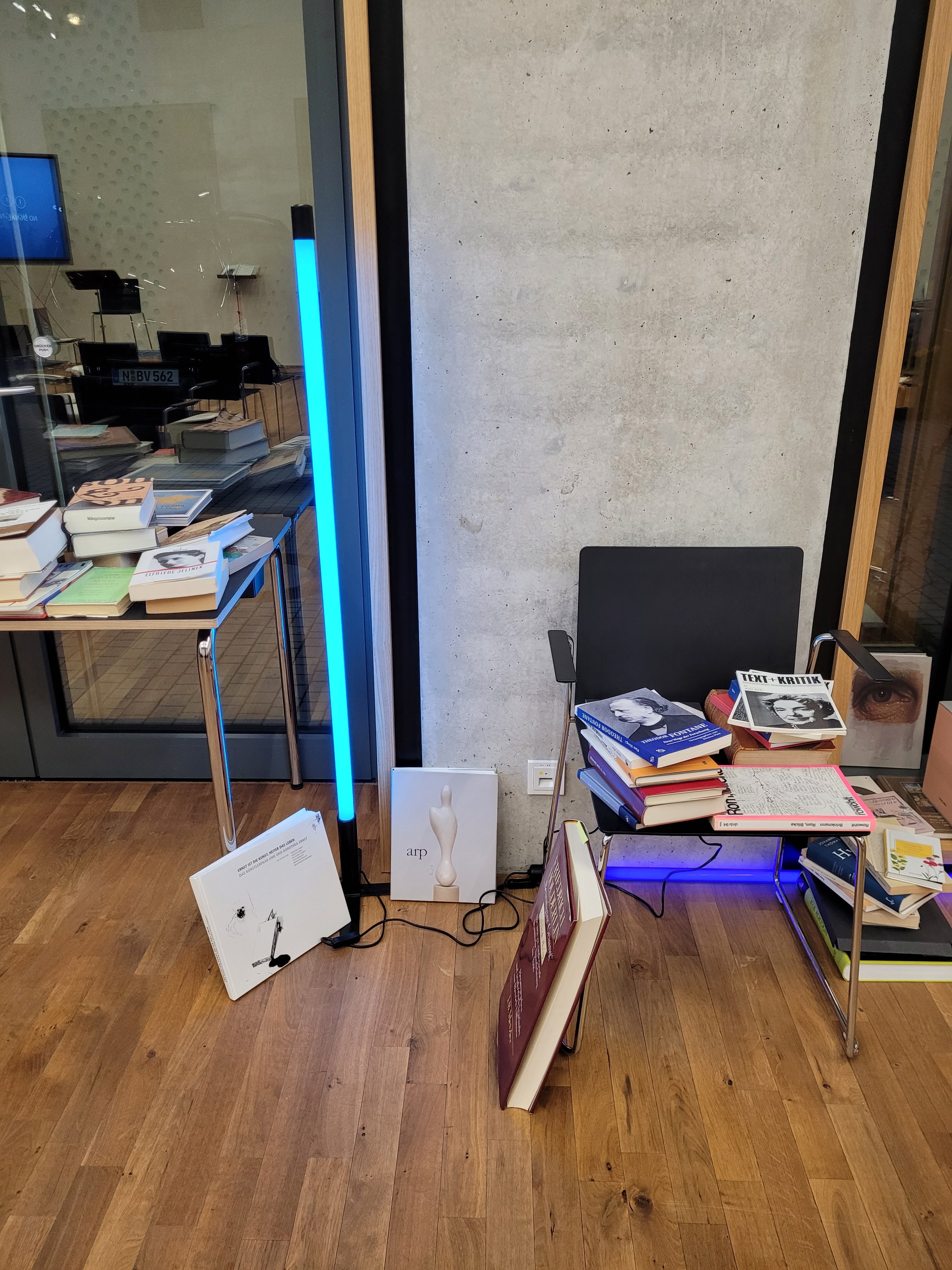 Bücher, wild drappiert auf Tisch und Stuhl in der Mitte eine blaue Leuchtstoffrühe